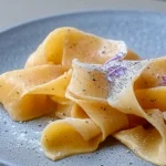 fresh pappardelle pasta nests on wooden bench