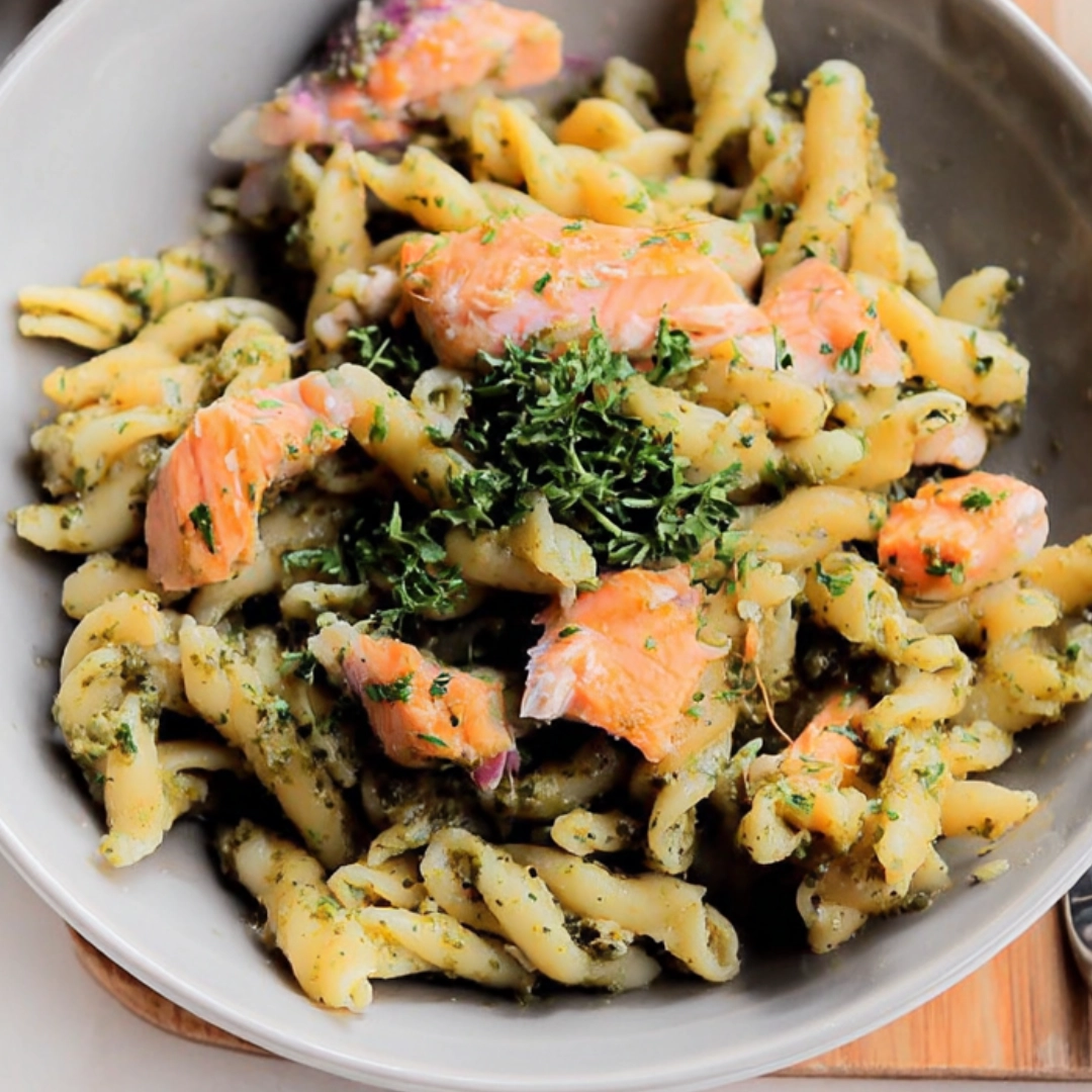 Penne pasta cooked in creamy pesto sauce, shown before and after adding grilled salmon chunks in a skillet Penne pasta cooked in creamy pesto sauce, shown before and after adding grilled salmon chunks in a skillet