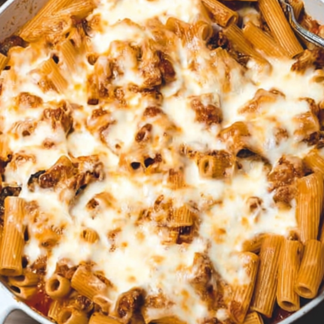 baked-rigatoni-in-casserole Baked rigatoni served in a white casserole dish topped with fresh herbs and melted mozzarella