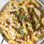A plate of creamy chicken bacon ranch pasta topped with fresh herbs