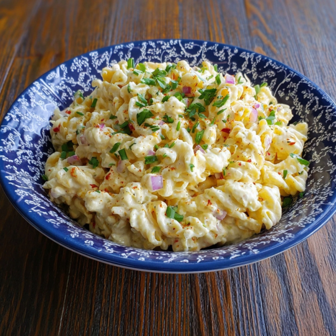 creamy-deviled-egg-pasta-salad-recipe.webp Creamy deviled egg pasta salad in a decorative blue serving dish with herbs and paprika on top