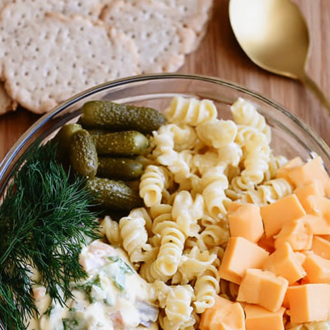 dill-pickle-pasta-salad-ingredients-bowl Bowl of dill pickle pasta salad ingredients including pickles, pasta, cheddar, dill, and dressing