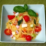 A close-up bowl of summer tagliolini pasta recipe with cherry tomatoes, basil, red onion and cucumber