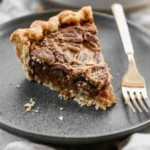 A perfect slice of rich homemade pecan pie recipe on a white plate with a side of vanilla ice cream.