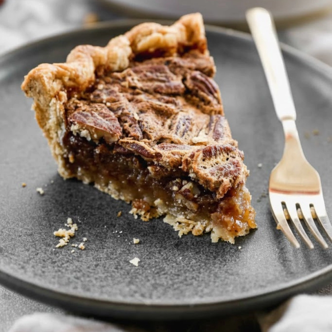 A perfect slice of rich homemade pecan pie recipe on a white plate with a side of vanilla ice cream.