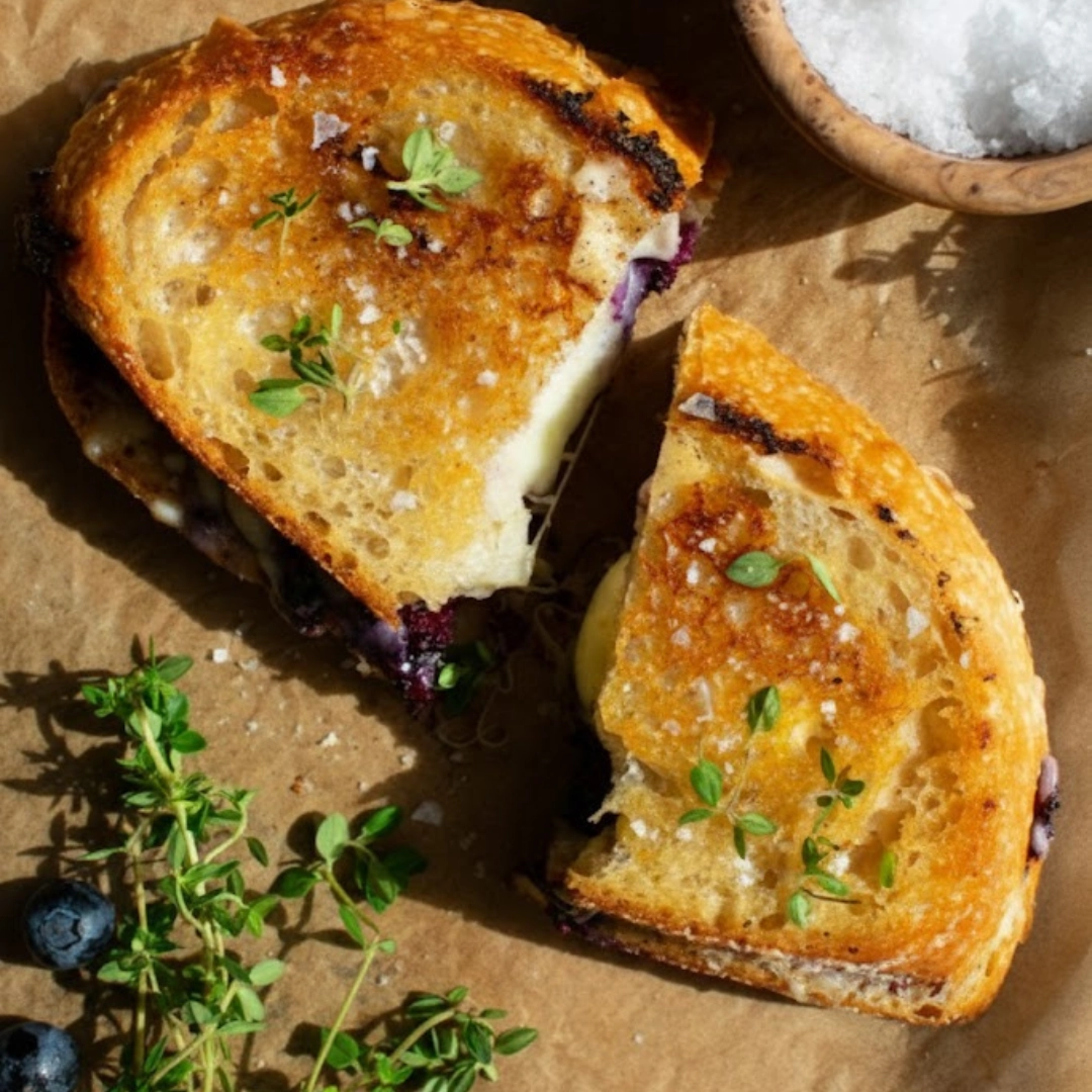 Stacked halves of a golden-brown Gourmet Blueberry Grilled Cheese showing the melted white cheddar and compote filling.