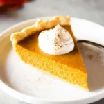 Slice of perfect homemade pumpkin pie on a plate with a dollop of whipped cream.