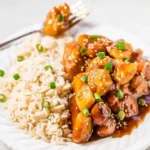 A full, glossy bowl of Slow Cooker Orange Chicken served over white rice, garnished with green onions.