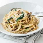 A large bowl of glossy, finished bucatini pasta recipe tossed in a bright garlic butter sauce with fresh parsley