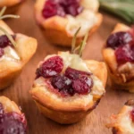 Close-up of golden brown Baked Cranberry Brie Bites topped with fresh thyme and honey drizzle