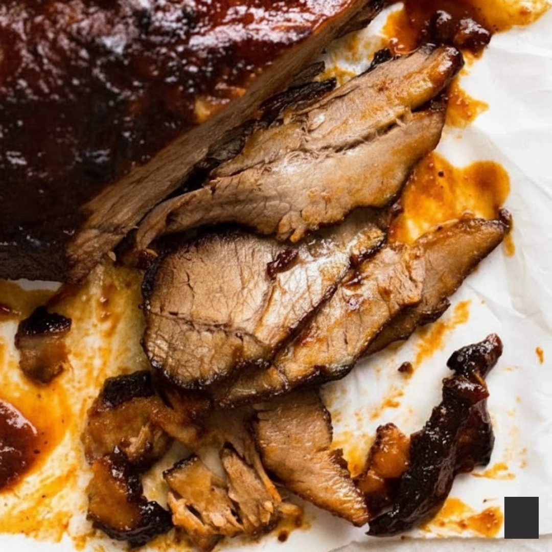 A plate of thinly sliced, fall-apart tender Slow Cooked Beef Brisket with BBQ sauce and side dishes.