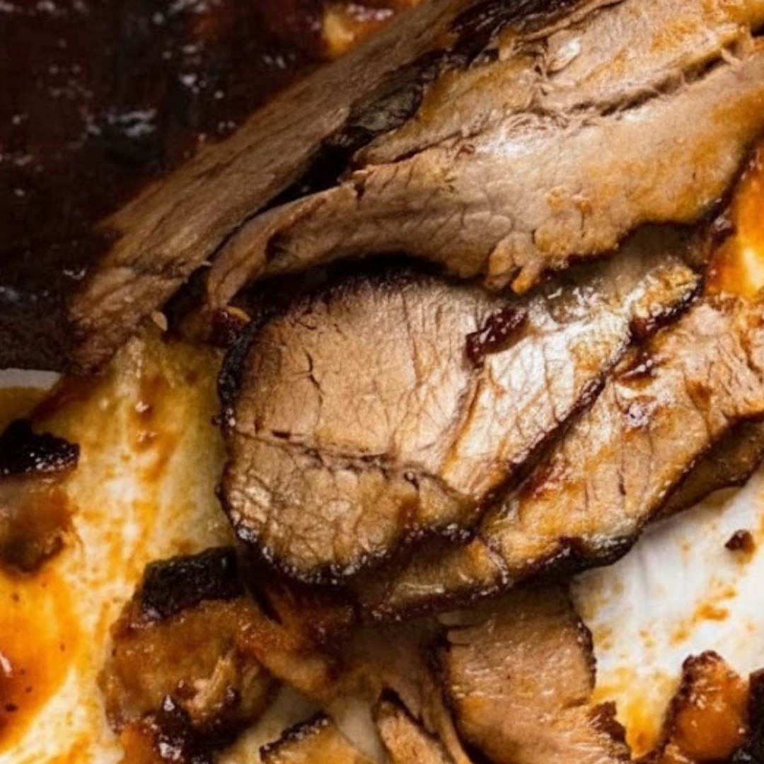 A plate of thinly sliced, fall-apart tender Slow Cooked Beef Brisket with BBQ sauce and side dishes. A plate of thinly sliced, fall-apart tender Slow Cooked Beef Brisket with BBQ sauce and side dishes.